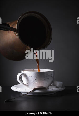 Hot black coffee poured from the coffee maker into a Cup . Old copper coffee maker and ceramic Cup with sugar cubes. Stock Photo
