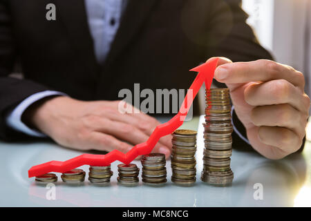 Close-up Of A Businessperson's Hand Holding Red Arrow Over Increasing Stacked Coins Stock Photo