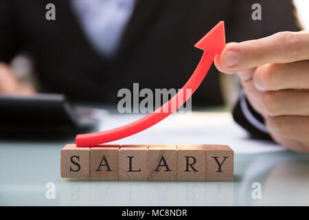 Close-up Of A Businessperson's Hand Holding Red Arrow Over Salary Blocks Stock Photo