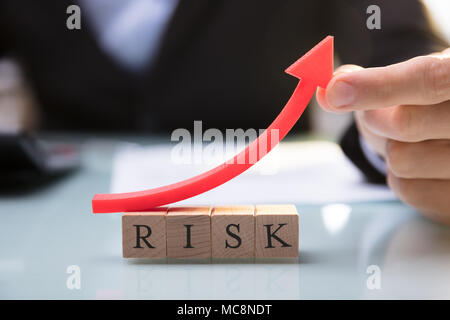 Close-up Of A Businessperson's Hand Holding Red Arrow Over Risk Blocks Stock Photo