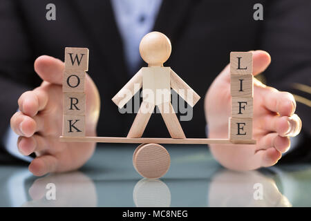 Close-up Of A Businessperson's Hand Protecting Balance Between Life And Work On Wooden Seesaw Stock Photo