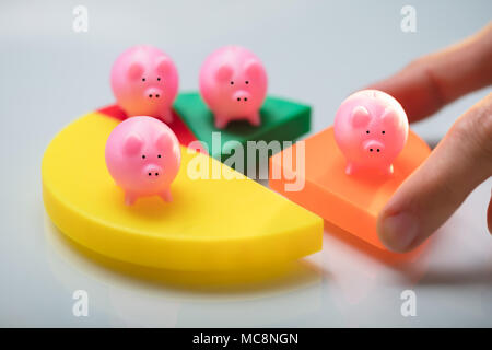 Person's Hand Placing Last Orange Piece Into Pie Chart With Small Pink Piggy Bank Stock Photo
