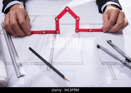 Architect's Hand Holding House Made With Red Measuring Tape On Blueprint Stock Photo