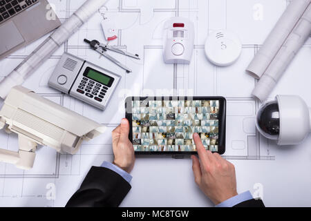 High Angle View Of A Person's Hand Holding Digital Tablet With CCTV Camera Footage Stock Photo