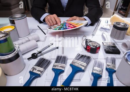 Architect's Hand Choosing Color From Swatch With Paint Brushes On Blueprint Stock Photo