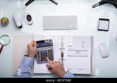 Elevated View Of A Businessperson's Hand Calculating Bill On Desk At Workplace Stock Photo
