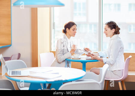 Two busy managers sitting by window in cafe, discussing online information and organizing work Stock Photo
