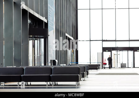 Waiting zone of modern airport with rows of black leather seats by large windows Stock Photo