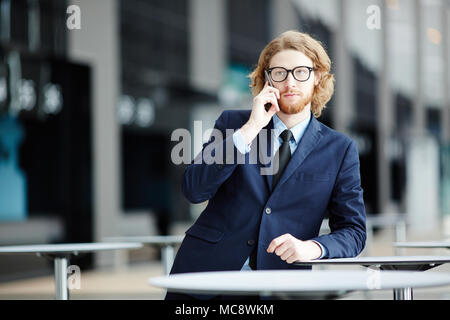 Serious businessman with smartphone making call to one of his clients or colleagues in airport Stock Photo