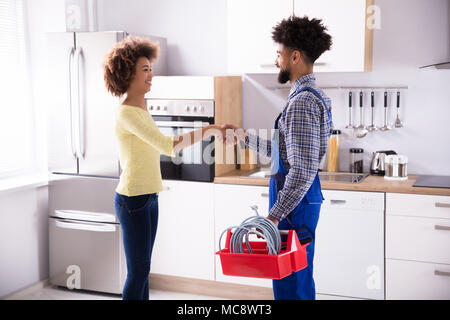 Side View Of Young Male Plumber Shaking Hands With Happy Woman Stock Photo