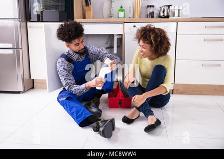 Plumber And Woman Sitting On Floor Looking At Damaged Sink Pipe Stock Photo