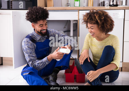 Plumber And Woman Sitting On Floor Looking At Damaged Sink Pipe Stock Photo