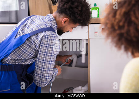 Woman Looking At Male Plumber Cleaning Clogged Pipes Stock Photo