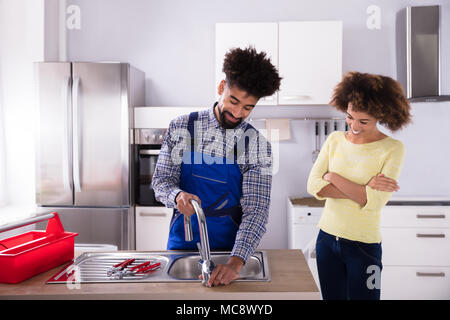 Happy Woman Looking At Male Plumber Fixing Faucet In Kitchen Stock Photo