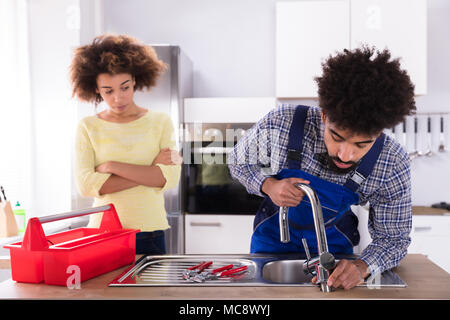 Happy Woman Looking At Male Plumber Fixing Faucet In Kitchen Stock Photo