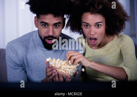 Shocked Couple Eating Popcorn While Watching Movie Stock Photo