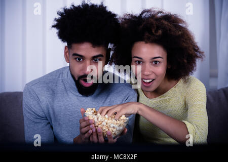 Shocked Couple Eating Popcorn While Watching Movie Stock Photo