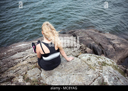 Rear view of a blond young woman sitting on a rock looking at view Stock Photo