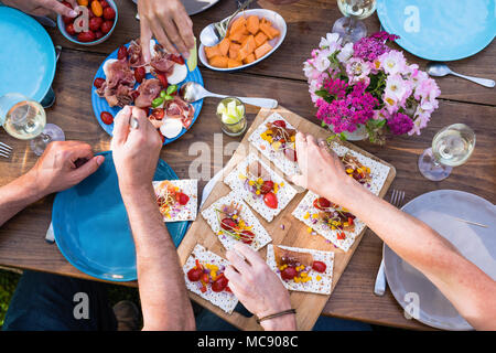 From above. a wooden table in the garden with food dishes and hands used for eating Stock Photo