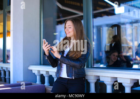 Young lady typing by smartphone at street cafe. Stock Photo