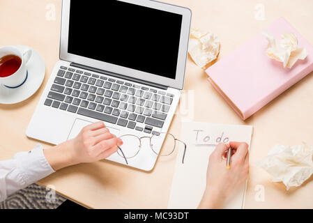 laptop on the table and female hands at work top view, writing in notebook Stock Photo