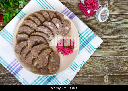 Home made dietary sausage from the liver on a wooden table. Sausage cut into pieces on a plate with horseradish sauce. Top view. Stock Photo