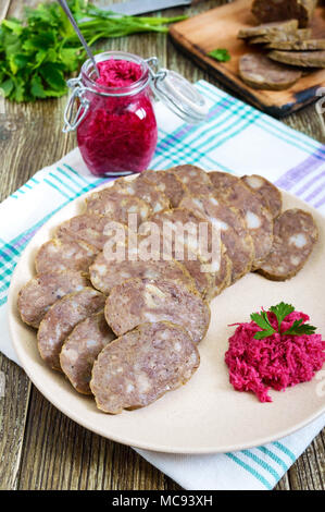 Home made dietary sausage from the liver on a wooden table. Sausage cut into pieces on a plate with horseradish sauce. Stock Photo