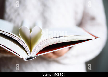 Book with opened pages and shape of heart in girl hands. Copy space. Love concept Stock Photo