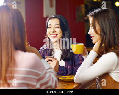 three happy beautiful young asian women sitting at table chatting talking in coffee shop or tea house. Stock Photo