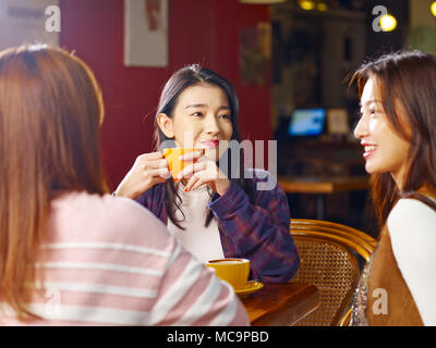 three happy beautiful young asian women sitting at table chatting talking in coffee shop or tea house. Stock Photo
