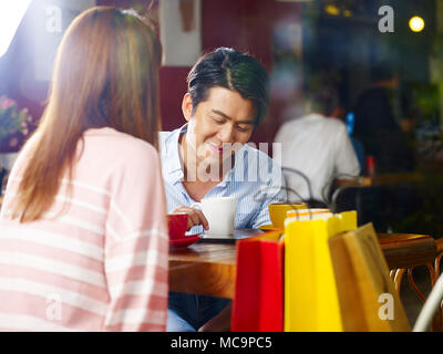young asian couple relaxing chatting talking in coffee shop after shopping, shot through window glass. Stock Photo