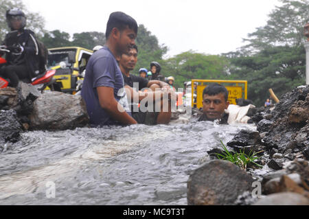 Bogor, Indonesia. 14th Apr, 2018. The water leak from pipe on jalan Harupat, Sempur, Bogor made some operators from Local Water Supply Utility busy. Because the leak was near Bogor Presidential Palace and the road is usually used by the President. Not only made a long traffic jam, this leak is also used by some people to wash their motorcycle. Credit: Andi Muh Ridwan/Pacific Press/Alamy Live News Stock Photo