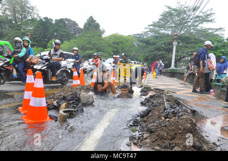 Bogor, Indonesia. 14th Apr, 2018. The water leak from pipe on jalan Harupat, Sempur, Bogor made some operators from Local Water Supply Utility busy. Because the leak was near Bogor Presidential Palace and the road is usually used by the President. Not only made a long traffic jam, this leak is also used by some people to wash their motorcycle. Credit: Andi Muh Ridwan/Pacific Press/Alamy Live News Stock Photo