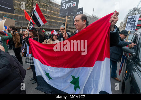 April 13, 2018 - London, UK. 13th April 2018. People block Whitehall in protest, holding a Syrian flag .Stop the War and Syrians protest at Downing St calling for Theresea May to stop her plans to bomb Syria with the USA and France following the reports of a chemical weapon attack there. Stop the War handed in a letter signed by MPs, trade unionists and others and held a rally on the opposite side of Whitehall, with speeches from Stop the War and other activists. Noisy chanting continued and many of those present crossed the road to protest outside Downing St before blocking both carriageways Stock Photo