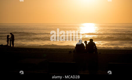 Families are silhouetted against the orange sea at sunset on the beach in Portugal in summer. Stock Photo