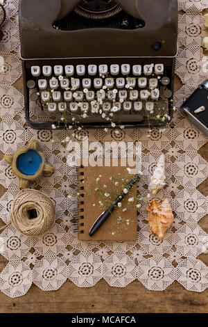 Spring or summer freelance, business or writing concept. Notepad with black pen on lace table cover with retro typewriter decorated with gypsophila fl Stock Photo