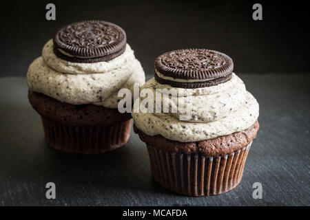 Two dark chocolate biscuit decorated chocolate sponge cup cakes close up on black background Stock Photo