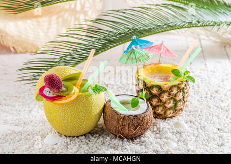 Drinks in fruits with cocktail umbrellas on white pebbles Stock Photo