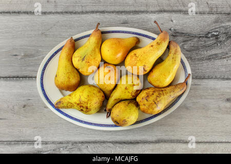 Table top view, green and yellow pears on oval plate with blue rim on gray wood desk Stock Photo