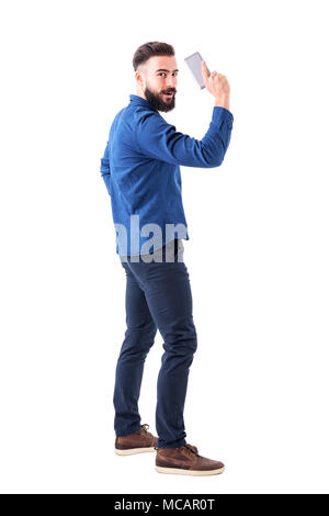 Playful young adult business man holding cellphone as handgun and looking at camera. Full body isolated on white background. Stock Photo