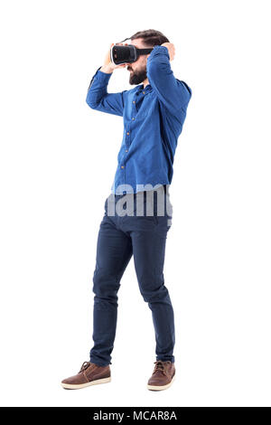 Side view of serious young bearded business man putting on virtual reality glasses. Full body length isolated on white background. Stock Photo