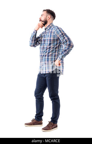 Young man in plaid shirt holding beard thinking and looking away. Side view. Full body isolated on white background. Stock Photo