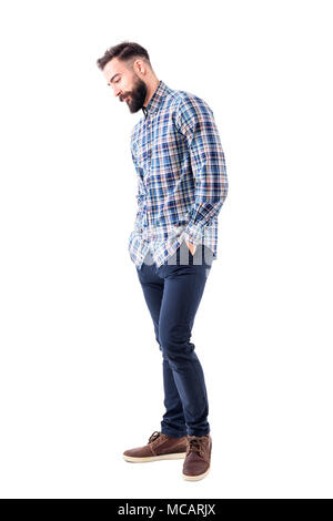 Shy handsome bearded young man in plaid shirt with hands in pockets smiling and looking down. Full body isolated on white background. Stock Photo