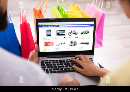 Close-up Of A Couple Shopping Online In Front Of Multi Colored Shopping Bags At Home Stock Photo