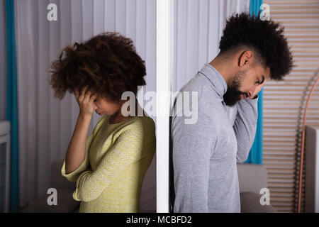 Side View Of Young Unhappy Couple Standing Back To Back At Home Stock Photo