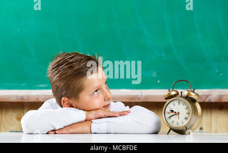Cute preschool boy with alarm clock awaiting for lesson Stock Photo