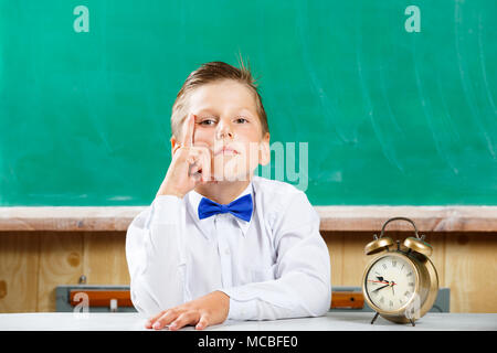 Cute school boy with alarm clock awaiting for lesson Stock Photo