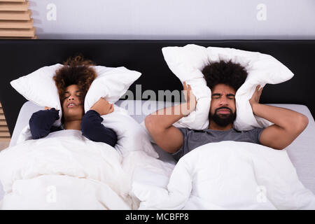 Elevated View Of Young Couple Lying In Bed Covering Their Ears With Pillow Stock Photo