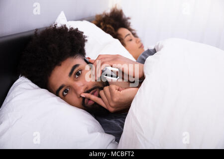 Young Man Talking Privately On Cell Phone While Her Wife Sleeping In Bed Stock Photo