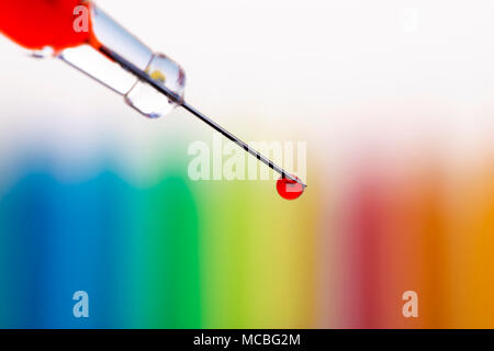 Macro of a single drop of blood hanging at the end of a syringe needle over blurred rainbow background. Shallow DOF. Stock Photo